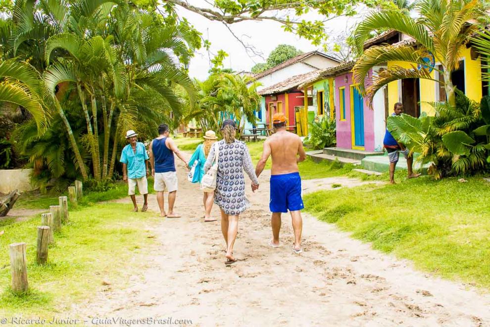 Imagem de turistas andando pelas ruas de areia na frente das casas coloridas.